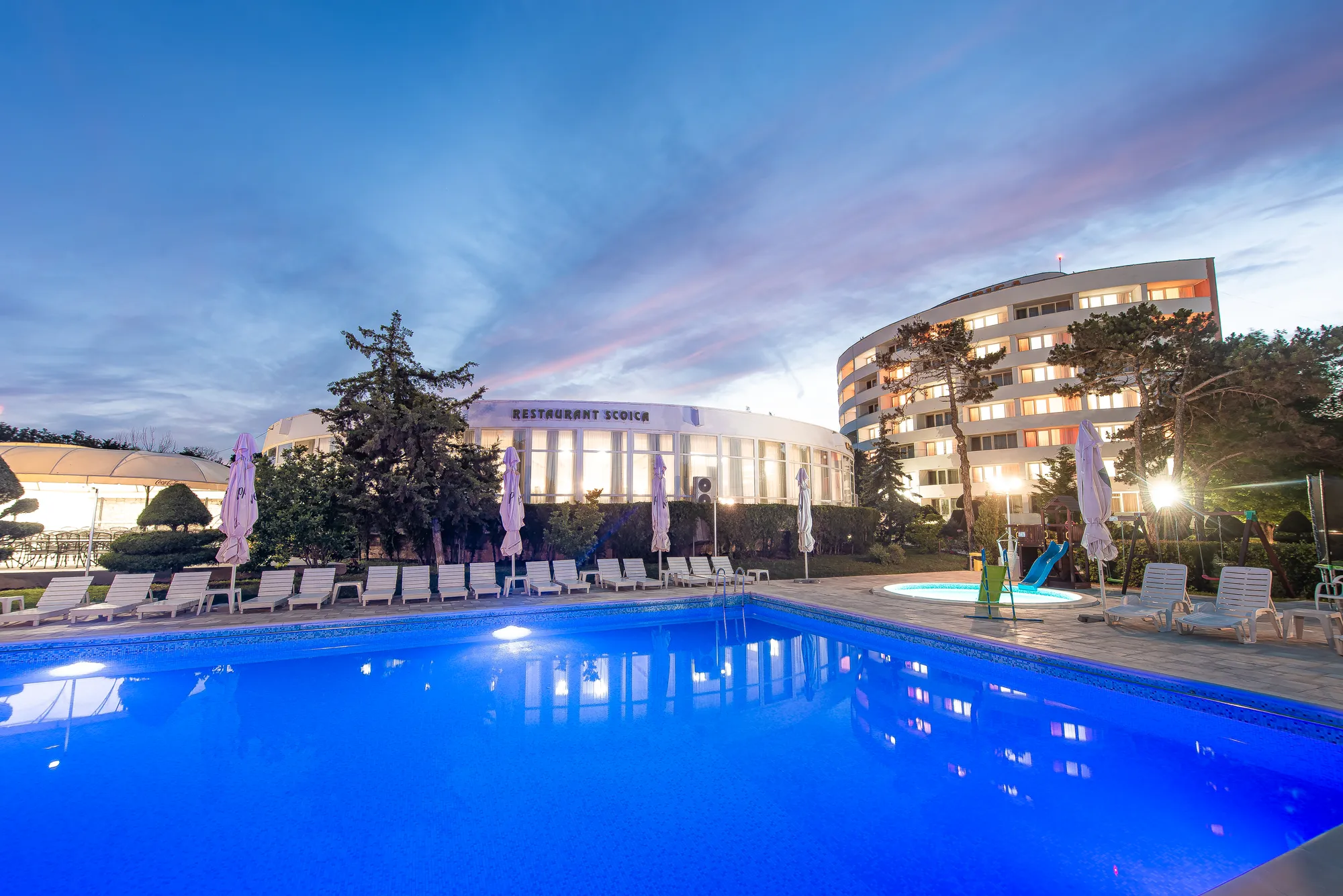 Piscina principală pe înserat, cu restaurantul iluminat în fundal