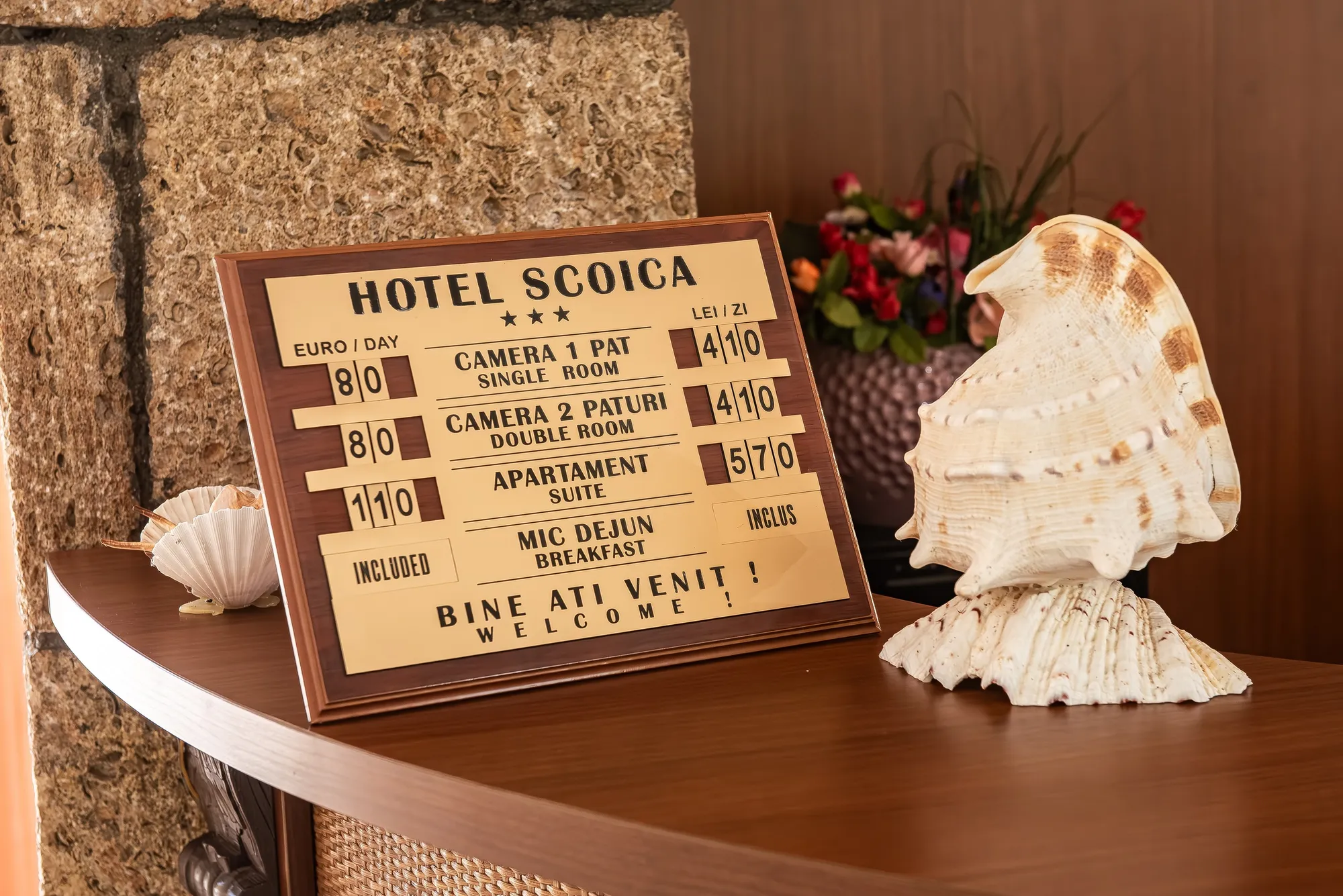 Panoul cu tarife Hotel Scoica, decorat cu scoici și flori